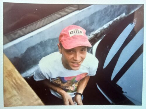 Tyler wearing a pink hat that says Gulf, smoking a cigarette.