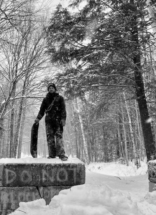 Willis standing in the snow, holding a skateboard deck.